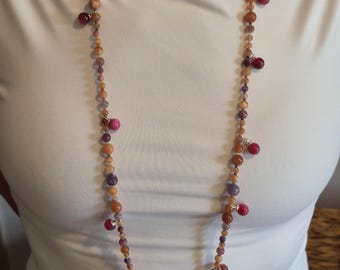 May include: A long beaded necklace featuring a strand of small, multi-coloured round beads in shades of amber, purple, and tan. The necklace is accented with larger, vibrant magenta spherical beads attached at intervals with silver-toned metal wire.