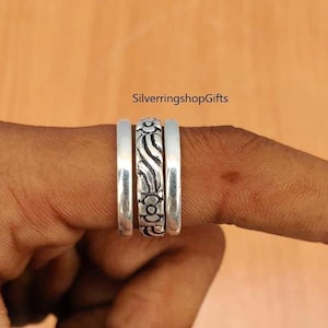 May include: A set of three silver rings worn together. The two outer rings have a smooth, polished finish, while the center ring features a detailed, repeating floral pattern with dark, recessed accents. The text SilverringshopGifts is visible.