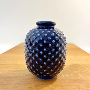 Può includere: Un vaso in ceramica blu profondo con una forma arrotondata e bulbosa e un collo stretto. La superficie esterna è ricoperta da un motivo denso e uniforme di borchie appuntite in rilievo che creano un aspetto strutturato su tutto il corpo.