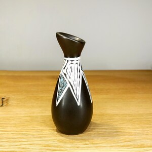 Peut inclure: Un petit vase marron foncé avec une forme unique et un motif décoratif. Le vase présente un dessus évasé et un corps en forme de goutte d'eau. Le motif comprend des motifs géométriques blancs et turquoise, ajoutant un intérêt visuel.