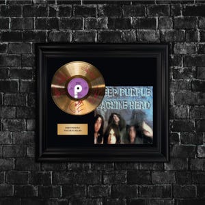May include: Framed gold record with signatures, featuring a purple and white label. The frame includes a Deep Purple "Machine Head" album cover and a gold plaque. The frame is black, set against a dark brick wall.