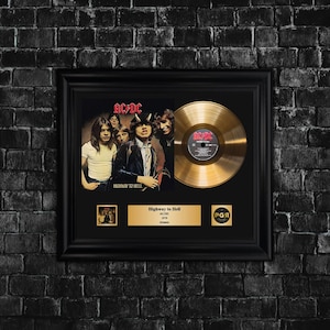 Op de afbeelding: Zwart omlijst AC/DC "Highway to Hell" album artwork en een gouden plaat. De albumhoes toont de bandleden. Onder de album artwork staat een gouden plaat met de albumtitel, artiest en jaar.