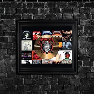 May include: Framed Metallica album art display. The black frame surrounds a collection of album covers and a gold-colored record with the band's logo and a skull graphic. The background is a dark brick wall.