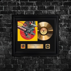 May include: Framed gold record and album art from the album "Screaming for Vengeance" by Judas Priest. The album art features a black and silver eagle over a red circle. The frame is black.