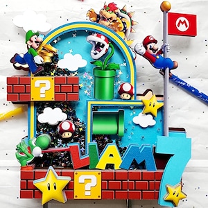 May include: A colorful cake topper featuring characters from the Super Mario Bros. video game. The design includes Mario, Luigi, Bowser, and other iconic elements like question mark blocks, stars, and a flag. The name "LIAM" and the number "7" are also included.