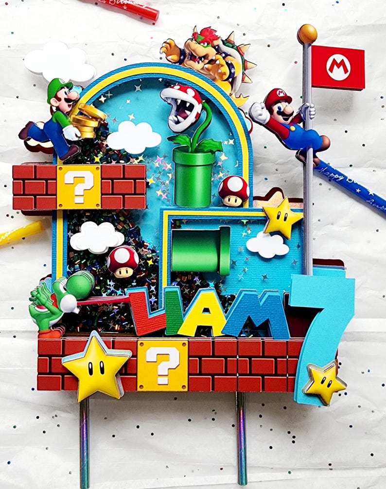 May include: A colorful cake topper featuring characters from the Super Mario Bros. video game. The design includes Mario, Luigi, Bowser, and other iconic elements like question mark blocks, stars, and a flag. The name "LIAM" and the number "7" are also included.