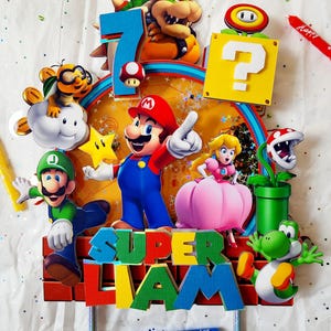 May include: A colorful Super Mario-themed birthday cake topper. The topper features Mario, Luigi, Princess Peach, Yoshi, Bowser, and other characters. The number 7 is displayed, along with the name "Liam" and the words "Happy Birthday".