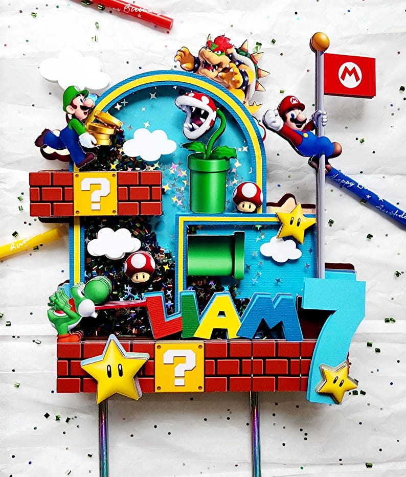 May include: A colorful birthday cake topper featuring characters from the Super Mario Bros. video game. The design includes Mario, Luigi, Bowser, Yoshi, and other iconic elements like question blocks, stars, and a flag. The name "LIAM" and the number "7" are also displayed.