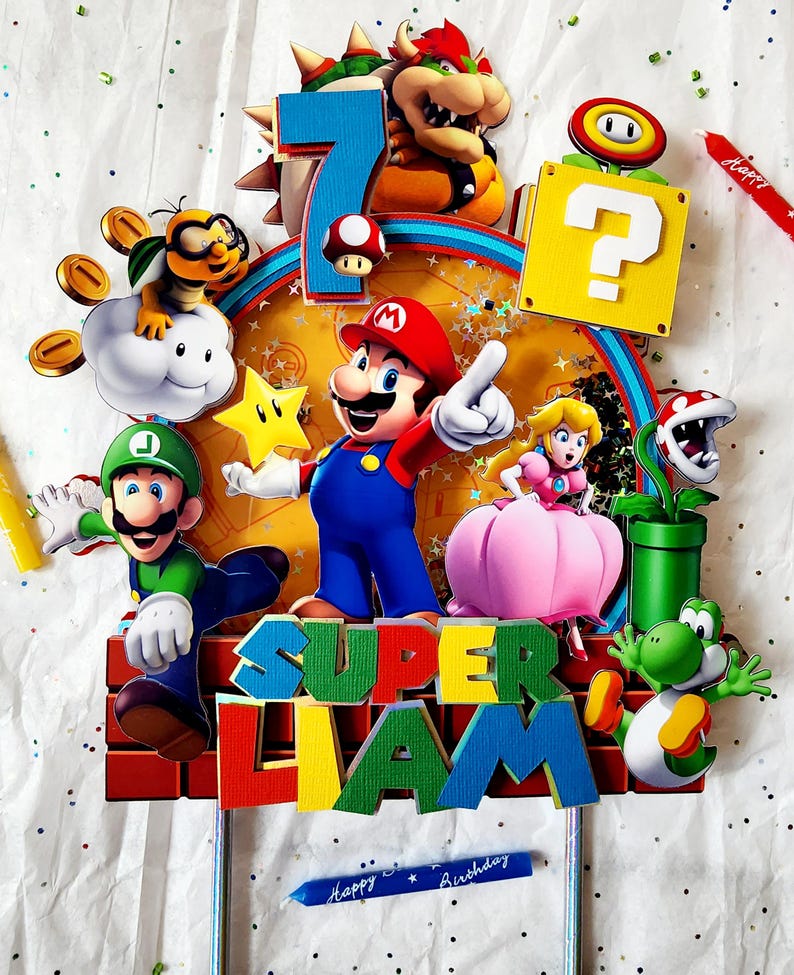 May include: A colorful Super Mario-themed cake topper featuring Mario, Luigi, Princess Peach, Bowser, Yoshi, and other characters. The topper includes the number 7, the name "Liam", and the words "Happy Birthday".