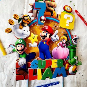 May include: A colorful Super Mario-themed cake topper featuring Mario, Luigi, Princess Peach, Yoshi, and Bowser. The number 7 is displayed, along with the name "Liam" and the words "Happy Birthday". Includes a question block, coins, and a star.