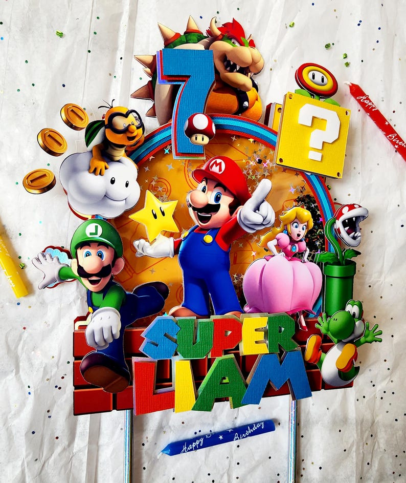 May include: A colorful Super Mario-themed cake topper featuring Mario, Luigi, Princess Peach, Yoshi, and Bowser. The number 7 is displayed, along with the name "Liam" and the words "Happy Birthday". Includes a question block, coins, and a star.