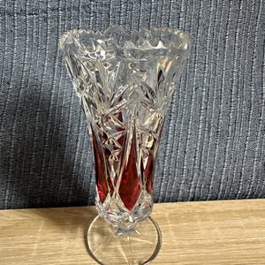 Könnte beinhalten: Eine Vase aus klarem und rubinrotem Schliffglas mit einem ausgestellten, gezackten Rand und einem Standfuß. Der Körper der Vase zeigt komplexe geometrische Muster mit abwechselnden klaren und tiefroten Feldern in einem facettierten Design.
