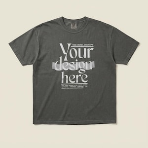 May include: A dark grey t-shirt featuring the text "Your design here" in a decorative font. The text is partially obscured by a translucent ribbon effect. The shirt is a mockup, designed to showcase design placement. The t-shirt has a vintage appearance.