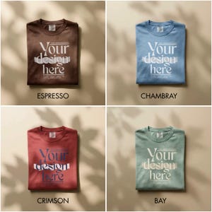 May include: Four folded t-shirts in espresso, chambray, crimson, and bay colors. Each shirt features the text "Your design here" in a stylized font. The shirts are displayed on a neutral background with soft shadows.