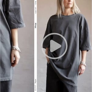 May include: A dark gray, oversized t-shirt with short sleeves. The shirt is worn by a person. The model is 5'4" and 112 lbs. The shirt is a 2XLarge size. The shirt is part of the Pepper collection, style CC1717.