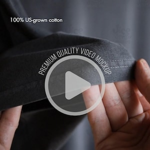 Puede incluir: Primer plano de una camiseta gris oscuro con el texto "100% US-grown cotton". El dobladillo de la camiseta es visible, con las palabras "PREMIUM QUALITY VIDEO MOCKUP" alrededor de un icono de reproducción.