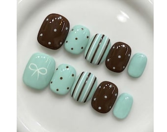 May include: A set of ten press-on nails featuring a color palette of chocolate brown and mint green. The designs include solid mint green, brown with white polka dots, mint green with brown polka dots, and vertical brown and white stripes on mint.