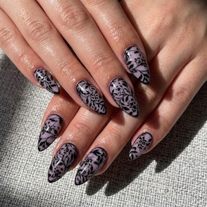 May include: Almond-shaped fingernails featuring a light lavender base color with a detailed black floral lace pattern overlay. The intricate botanical design covers the entire surface of each nail, creating a cohesive and decorative appearance across all ten fingers.