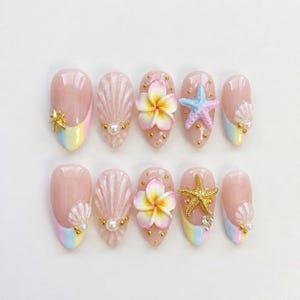 Könnte beinhalten: Zehn künstliche Fingernägel mit hellrosa Basis und Stranddekorationen. Die Designs umfassen Muscheln, Seesterne und Plumeria-Blüten. Jeder Nagel hat eine pastellfarbene Regenbogenspitze.