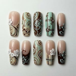May include: A set of ten press-on nails featuring a variety of designs in shades of brown, cream, and mint green. The nails include intricate floral patterns, swirling lines, plaid motifs, and three-dimensional white flower embellishments.