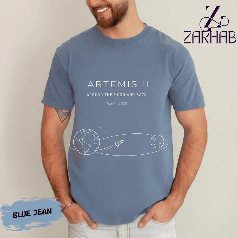 May include: Blue jean-colored t-shirt with the text "ARTEMIS II" and "AROUND THE MOON AND BACK" with a graphic of Earth, a rocket, and the moon. The date "April 1, 2026" is also printed on the shirt.