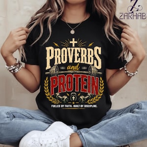 Puede incluir: Una camiseta negra de manga corta con un diseño gráfico que incluye el texto "PROVERBS and PROTEIN" en letras grandes amarillas y rojas. El diseño muestra una barra de pesas, mancuernas, una pesa rusa, una cruz y el texto "FUELED BY FAITH. BUILT BY DISCIPLINE."