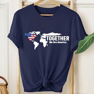 Puede incluir: Camiseta azul marino con un mapa del mundo blanco, que incorpora la bandera estadounidense en el continente de América del Norte. La palabra "TOGETHER" está impresa encima de "We Are America" en blanco, creando un diseño patriótico.