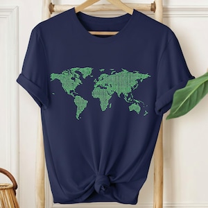 Puede incluir: Camiseta azul marino con un diseño de mapa del mundo verde. El mapa está compuesto por un patrón repetitivo de pequeñas formas. La camiseta tiene mangas cortas y está anudada a la cintura. Cuelga de una percha de madera.