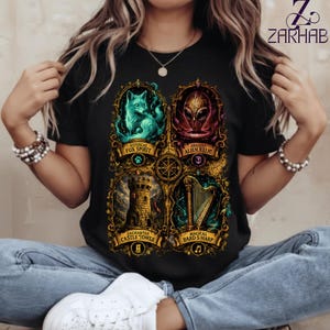 Puede incluir: Una camiseta negra con un estampado gráfico de cuatro paneles ornamentados con marcos dorados. Los paneles muestran un espíritu de zorro turquesa, una reliquia alienígena roja, una torre de castillo de piedra y un arpa dorada con etiquetas de texto.