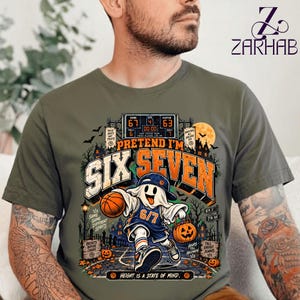 Puede incluir: Una camiseta verde oliva con un gráfico de un fantasma con camiseta y gorra de baloncesto, sosteniendo un balón y una calabaza. El diseño incluye un marcador que muestra 67 a 63, el texto "PRETEND I'M SIX SEVEN" y siluetas de árboles.