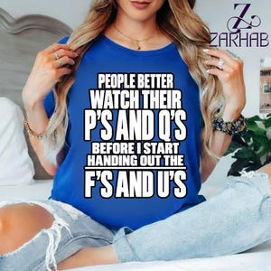 Peut inclure: Un t-shirt bleu roi à manches courtes avec un texte blanc en gras qui dit : PEOPLE BETTER WATCH THEIR P'S AND Q'S BEFORE I START HANDING OUT THE F'S AND U'S. Le t-shirt présente une encolure ronde et une coupe standard.