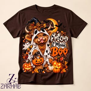 Puede incluir: Una camiseta marrón oscuro con el gráfico de una vaca Highland con disfraz de fantasma y sombrero de bruja. La vaca sostiene un cubo de calabaza con dulces. El texto dice Moo I Mean Boo, rodeado de calabazas, hojas de otoño y murciélagos.