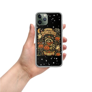 Puede incluir: Una funda de smartphone negra con una ilustración central de un mapache con sombrero de bruja y pañuelo, rodeado de calabazas, fantasmas y gatos. El texto dice HAPPY HALLOWEEN y STAY SPOOKY sobre un fondo de estrellas blancas.