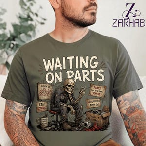 Könnte beinhalten: Ein olivgrünes T-Shirt mit einer Grafik eines Skeletts, das auf einem Hocker sitzt, und dem Text WAITING ON PARTS. Das Design enthält einen Kalender, eine Kaffeetasse, einen Karton mit der Aufschrift FRAGILE MY PATIENCE sowie Schilder mit den Texten PARTS ON THE WAY (MAYBE) und ETA SOMEDAY.