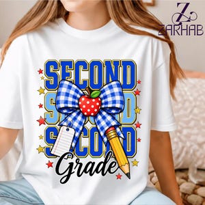 Puede incluir: Una camiseta blanca con un diseño gráfico que incluye el texto "SECOND GRADE" en letras azules. El diseño presenta un lazo a cuadros azul y blanco, una manzana roja con puntos blancos, un lápiz amarillo y una pequeña etiqueta de papel blanco.