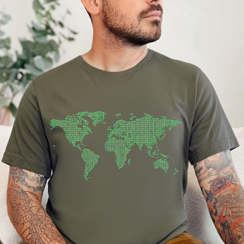 May include: Olive green t-shirt featuring a world map design made of green binary code. The graphic covers the front of the shirt, depicting continents and islands. The shirt is a casual, short-sleeved style.