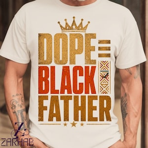 Puede incluir: Una camiseta de manga corta color crema con un estampado gráfico desgastado. El diseño incluye una corona dorada sobre el texto DOPE en oro, BLACK en naranja y FATHER en oro, con un patrón geométrico vertical y tres estrellas pequeñas.