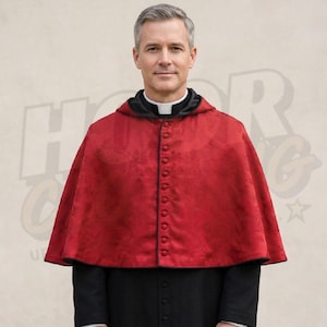 May include: A red hooded cape with a button-down front. The cape has a black trim and is worn over a black garment. The person in the image is wearing a white clerical collar.