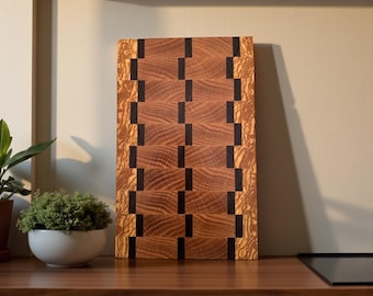 May include: A rectangular wooden cutting board with a geometric pattern. The board features alternating sections of light and dark brown wood, with black accents. The cutting board is displayed on a wooden countertop.
