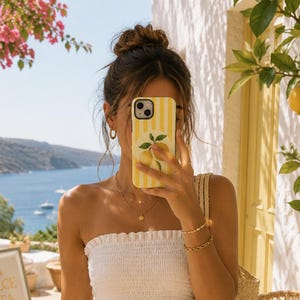 Peut inclure: Une femme porte un haut tube blanc et un short à carreaux jaunes. Elle tient un téléphone avec une coque à rayures jaunes et un motif de citron. Un sac fourre-tout en paille est sur son épaule. La scène est en extérieur avec une enseigne "La Dolce Vita".