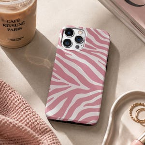 Peut inclure: Une coque de smartphone arborant un motif de rayures zébrées rose et blanc. La coque présente une découpe pour un système de caméra à trois objectifs au dos. Le design recouvre toute la surface arrière du téléphone avec un motif animalier.