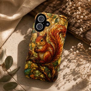 Peut inclure: Une coque de smartphone présentant une illustration détaillée d'un écureuil roux tenant un gland tout en étant perché sur une branche d'arbre. L'œuvre affiche une palette de couleurs automnales vibrantes avec des tons orange, brun, jaune et vert.