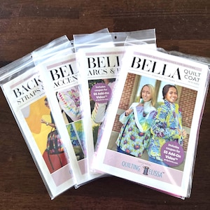 May include: Four sewing pattern packets in clear plastic sleeves. The packets feature the word "BELLA" in large letters, with titles like "QUILT COAT" and "BACK STRAPS". Each packet has images of quilted garments and includes a coupon for a video.