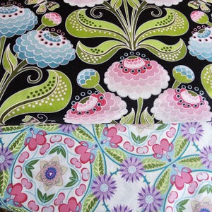 May include: Two fabric swatches with floral patterns. The top swatch is black with green leaves and pink, white, and blue flowers. The bottom swatch is white with green leaves and pink, purple, and blue flowers.