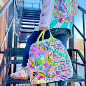 Può includere: Uno zaino colorato con un'illustrazione di gatto, scarpe abbinate e una giacca. Lo zaino presenta un design a gatto con accenti rosa, verdi e blu. Le scarpe e la giacca hanno un motivo simile. Il testo "Quilting Elissa" è visibile.