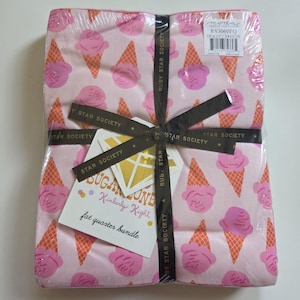Op de afbeelding: Een fat quarter stoffenbundel met een herhalend patroon van roze ijsbolletjes in oranje wafelhoorntjes op een lichtroze achtergrond. De bundel is omwikkeld met een zwart lint met het label Ruby Star Society en bevat een label met de tekst Sugar Cone.