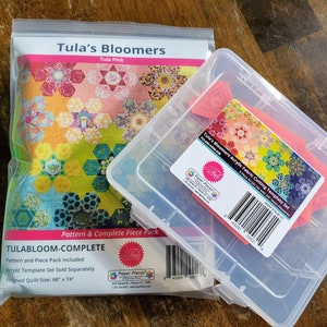 May include: A clear plastic bag containing a quilting pattern and fabric pieces for a quilt called "Tula's Bloomers" in the colour "Tula Pink". The pattern includes a complete piece pack and the finished quilt size is 68 inches by 74 inches. A clear plastic storage container with a pink label that says "Tula's Bloomers Acrylic Fabric Cutting Template Set" is also included.