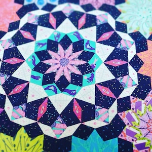 Pode incluir: Um cobertor colorido com um padrão geométrico de estrelas e outras formas. O cobertor é feito de vários tecidos com diferentes estampas, incluindo rosa, azul e branco.