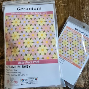 May include: A close-up of two packages containing a quilting pattern and template set for a "Geranium" quilt. The pattern is by Elouise O'Hare and is called "Geranium-Baby". The finished quilt size is 31-1/5 inches by 45 inches.