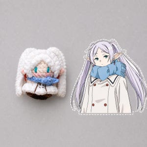 May include: A small crochet doll with white hair and a blue scarf next to a flat, die-cut sticker of an anime character with long light purple hair, pointed ears, a blue scarf, and a white coat with brown buttons, matching the doll's appearance.